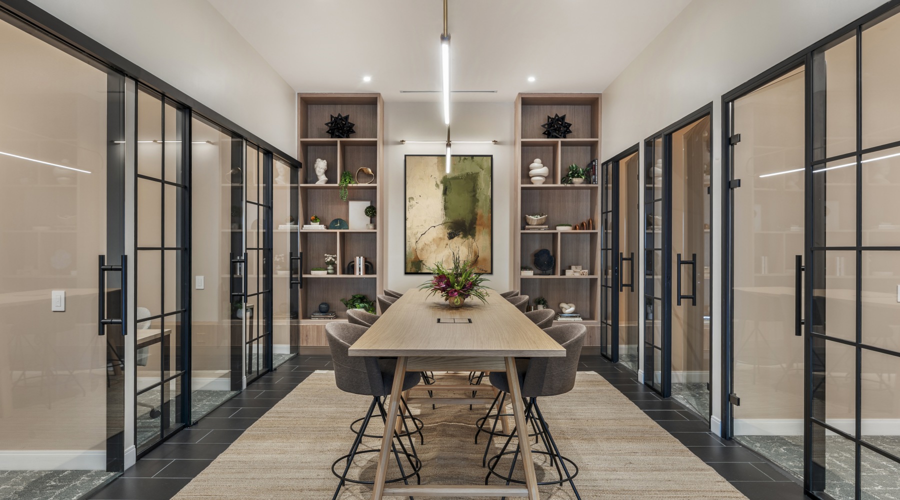 Modern coworking lounge at 75 Tresser apartments in Stamford with a long communal work table and glass-enclosed meeting spaces.
