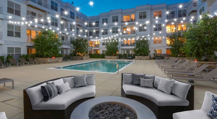 Pool area at our apartments for rent in Stamford, CT, featuring outdoor couches, a fire pit, and string lights.