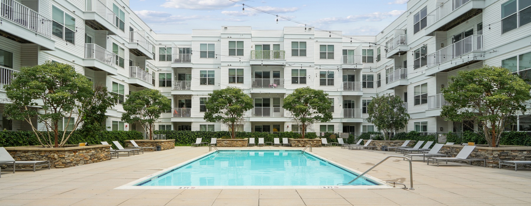 Swimming pool in a courtyard surrounded by lounge seating and an apartment building in the background