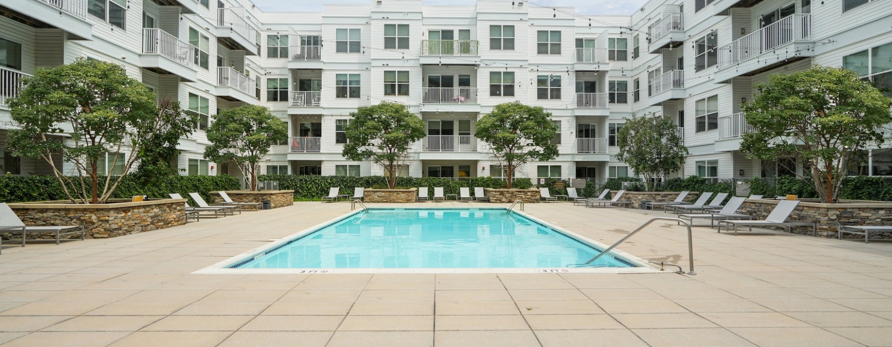 The pool area featuring beach chairs, trees, and a view of the apartments at our apartments for rent in Stamford, CT.