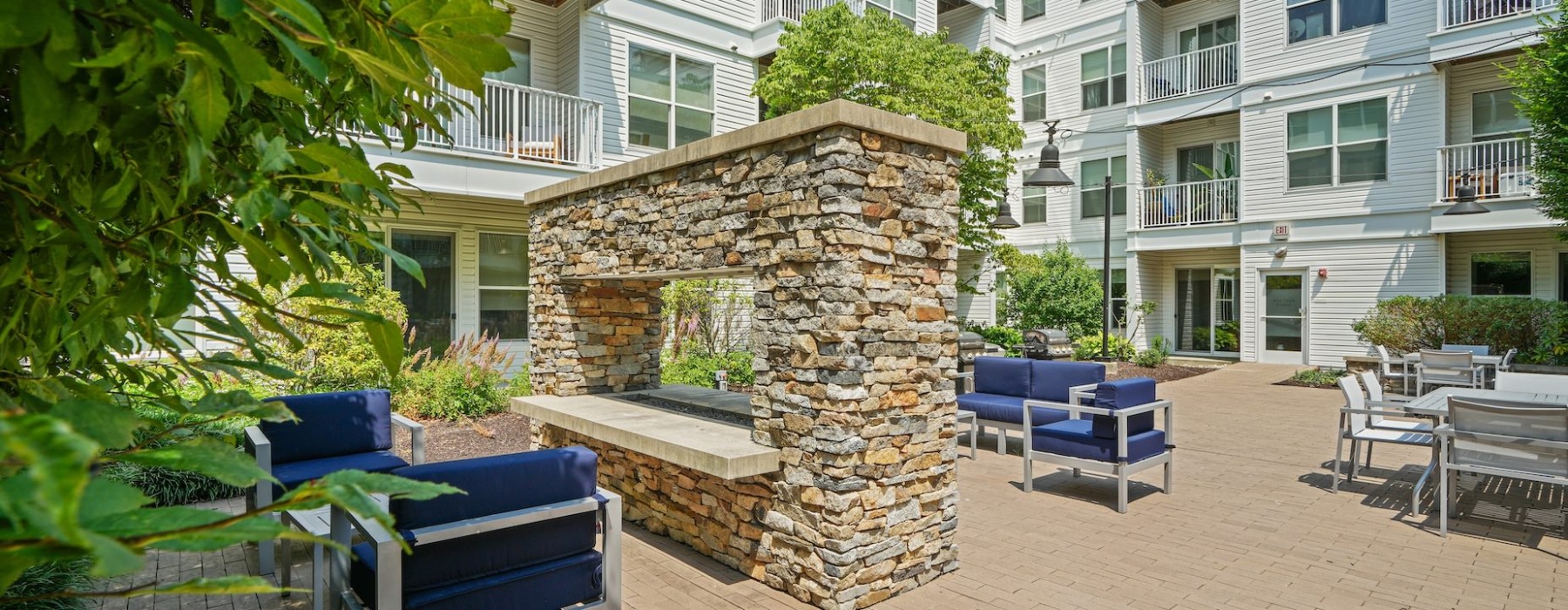 a courtyard with an outdoor fireplace and cushioned outdoor chairs and view of apartment building in background